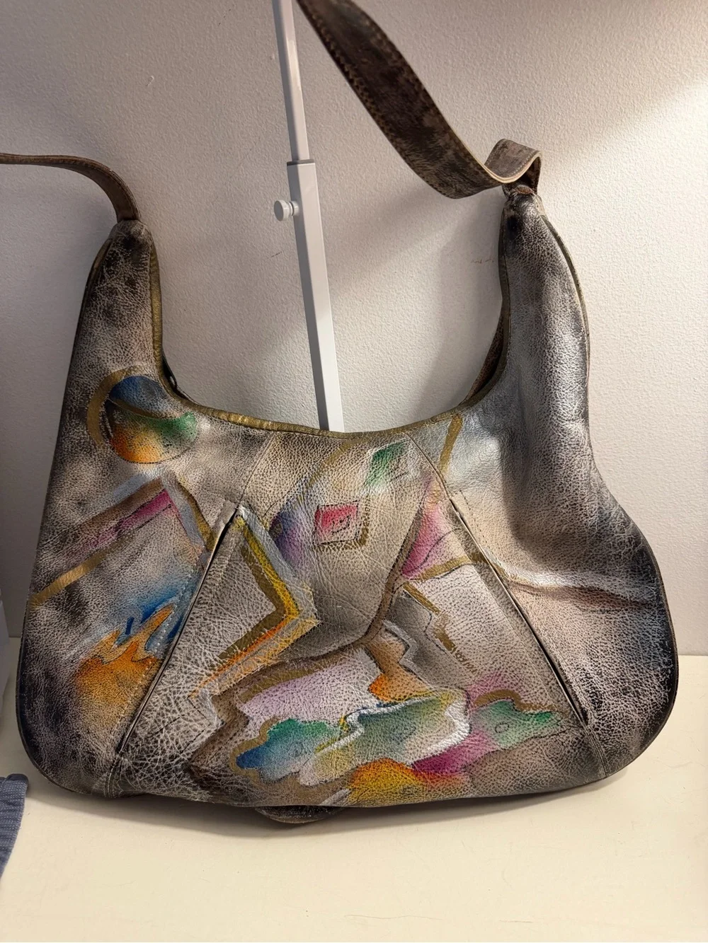 Distressed leather hobo bag with colorful abstract design on front and back.